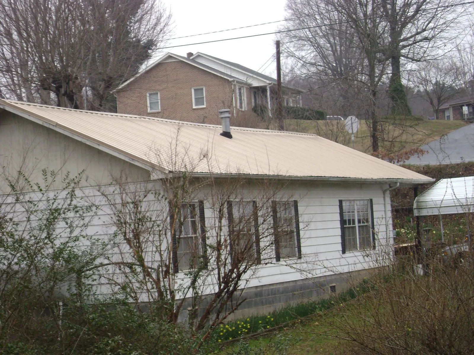 Tan metal roof on a white sided house set into a hillside — Commercial Roofing by Roofing Brothers in Walkerton