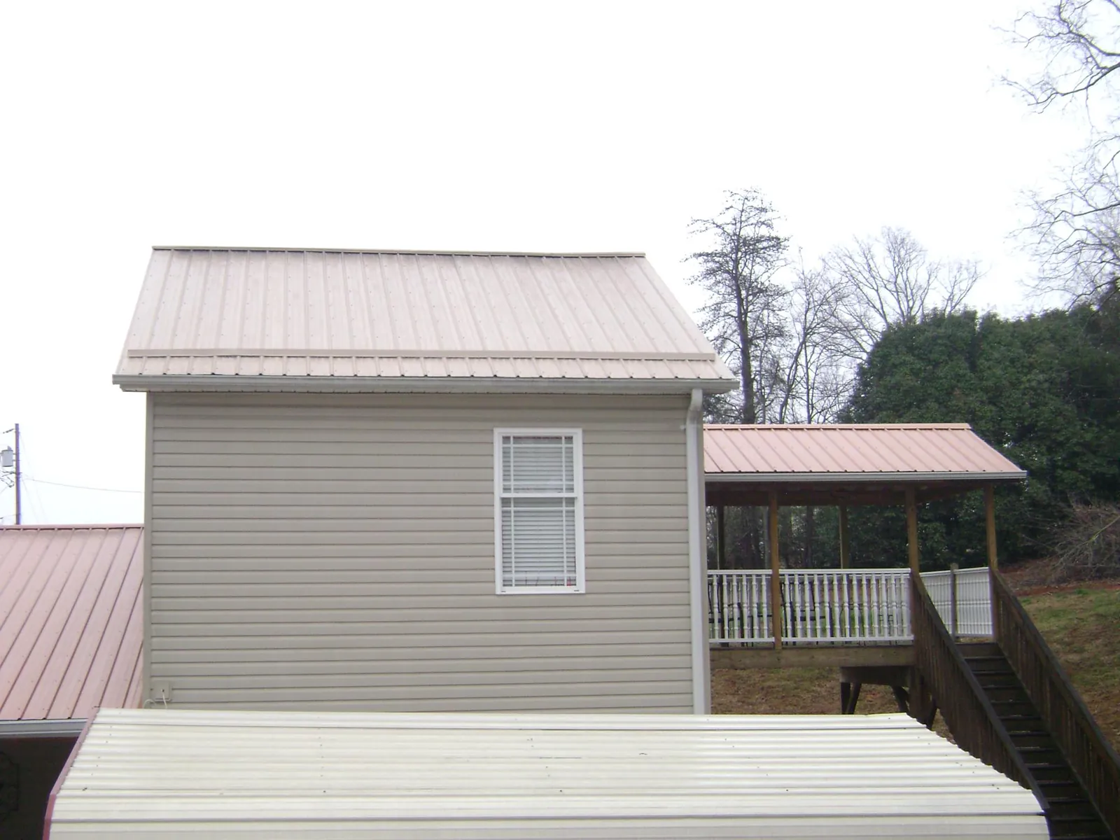 Tan metal roofs on a two story addition and attached porch, from a Roof Replacement job in Walkerton